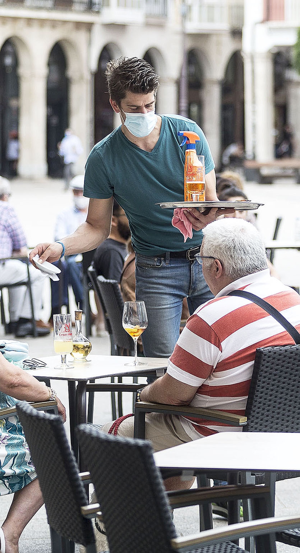 2 · Javier, de la Tapería del Casino en la Plaza Mayor, entrega la cuenta a unos clientes a la vez que lleva en la bandeja los productos de limpieza.  / CHRISTIAN CASTRILLO