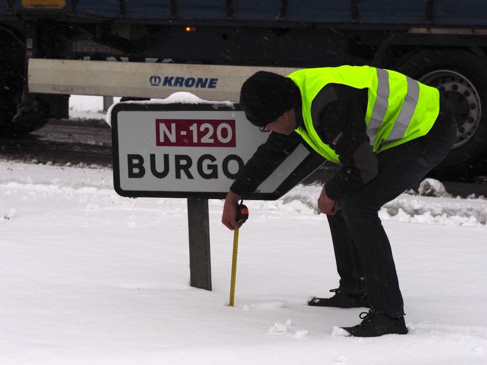 Un camionero saca el metro para medir la capa de nieve caída sobre la N-120.
