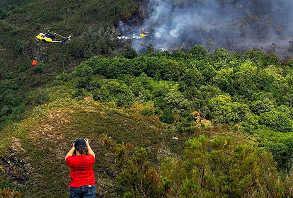 Una mujer fotografía dos hidroaviones que participan en la extinción de un fuego en Galicia.