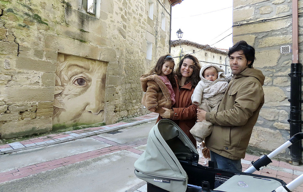 Esther González y Octavio Macías con sus hijos junto al mural de un anciano pintado por él.