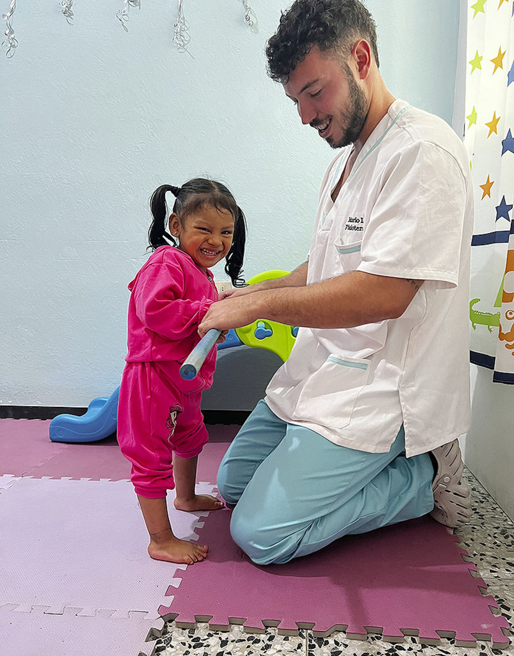 Mario López ayuda a una pequeña paciente a mantenerse de pie. 